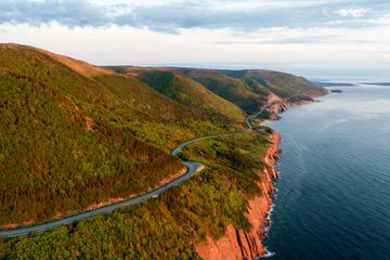 Aerial view of the Cabot Trail on Cape Breton Island, with the road winding through the forest next to the shoreline