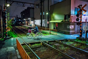 A cyclist crosses train tracks near Osaka’s Tengachaya Station, at night