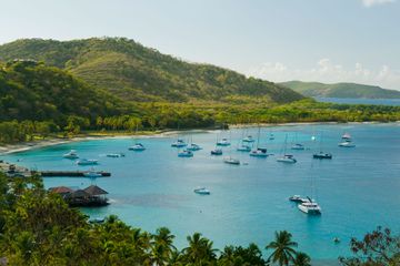 Aerial view of Britannia Bay, Mustique. Plenty of small yachts on blue water, green hills and blue sky in the background.