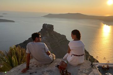 A couple sitting on a rock watching the sunset in Santorini