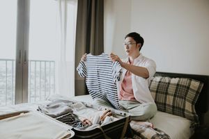 Asian man packing her clothes into a suitcase, getting ready for a trip.