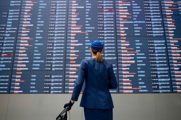 Portrait of a flight attendant at the airport checking an arrival departure board and carrying her luggage