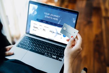 Cropped shot of young woman booking flight tickets on airline website online with laptop, entering credit card details to make online payment at home. Travel planning. Booking a holiday online. Travel and vacations concept. Business trip planning - stock photo