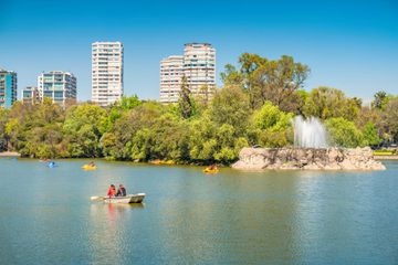 People relax on Lago Menor in Chapultepec Park, Mexico City, Mexico on a sunny day, with view towards Polanco district.