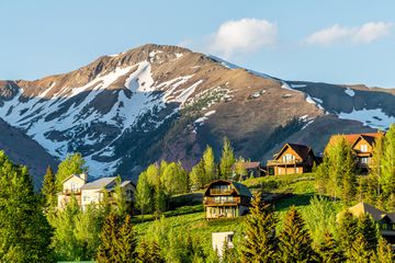 Mount Crested Butte Colorado village in summer with colorful sunset by houses on hills with green trees and main street road