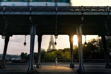 A person stands in the sunlight under a bridge while viewing the Eiffel Tower in Paris