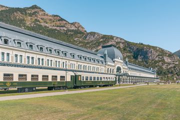 The exterior of a hotel and train with a mountain in the background.