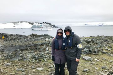 A man and woman in Antarctica with a cruise ship in the background 