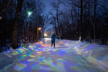 A woman skates down the Victoria Park IceWay lit with colourful lights at night 