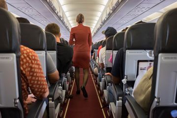 Flight attendant walks down aisle of aircraft full of passengers 