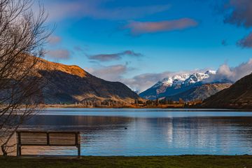 A bench overlooks a lake surrounded by mountains in New Zealand