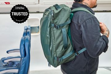 Person wearing Away The Outdoor Convertible Backpack 45L near airplane seats and overhead bins
