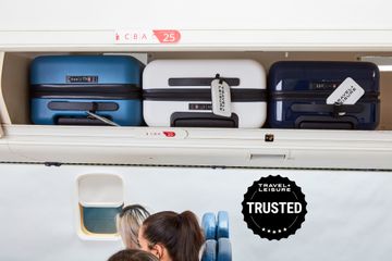 Three pieces of carry-on luggage in an airplane's overhead bin with passengers seated below
