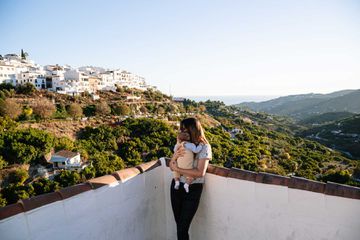Portrait of a young mother hugging her baby. Andalusian village with white houses and coast in the background