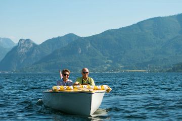 A happy and content senior age couple on a boat in a lake with mountains in the distance