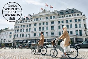 Two people ride bikes past a hotel in Copenhagen