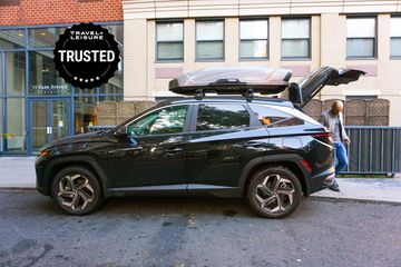 Thule Motion XT XL Roof Box attached to a CSUV parked along a sidewalk with the trunk open